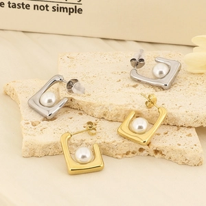 Detail of square gold and silver pearl earrings on a beige textured stone display