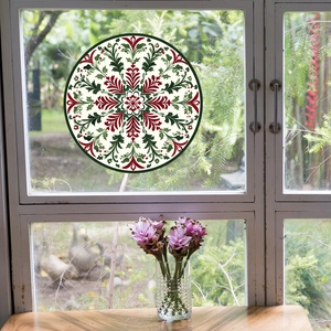 Detail of a festive red and green mandala window sticker on a glass pane with garden view