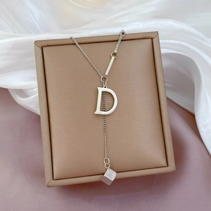 Minimalist silver necklace with letter D and cube pendant on an elegant jewelry box