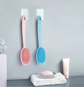 Pink and blue silicone bath brushes with long handles hanging on hooks in a bathroom