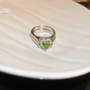 Macro detail of silver ring featuring a green heart-shaped gemstone and crystal halo