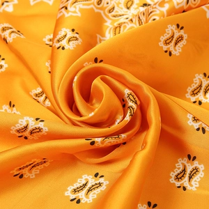 Macro shot of silk satin scarf featuring yellow paisley pattern and draped texture
