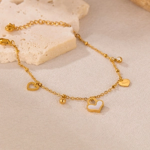 Makrofoto von goldenem Herzarmband mit Perlmutteinlage und Love Gravur Anhängern