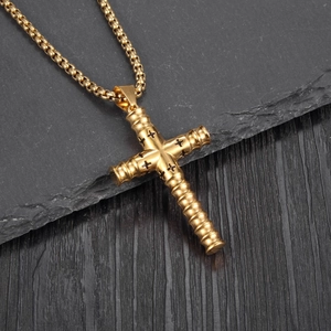Pendentif croix cylindrique doré vintage avec motifs noirs sur surface de pierre sombre