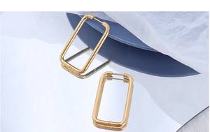 Polished 18k gold plated stainless steel rectangular hoop earrings on a reflective surface