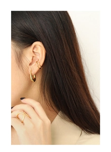 Close-up of golden nail cuff earring and minimalist curved ring on fashion model