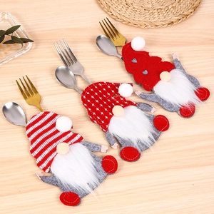 Three Christmas gnome cutlery holders with striped and star hats on a wooden table