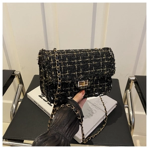 Close-up of black and gold tweed shoulder bag with metal turn-lock on luxury books