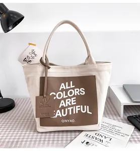 Detail of off-white canvas tote with brown leather patch and brand hangtag on a desk
