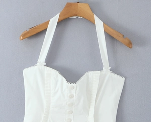 Close-up of white halter dress with front buttons, delicate lace trim and ruffle details