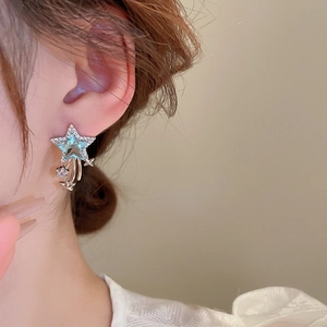 Close-up of elegant blue star crystal earrings with silver tassels on a model's ear