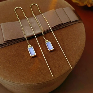 Detail of elegant gold linear earrings with purple rectangular oil-drop pendants