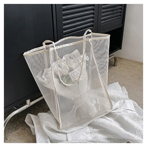 Detail of white mesh tote bag with double handles shown against a black shutter backdrop