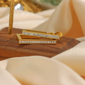 Macro view of gold-plated rectangular earrings with white rhinestones on satin fabric