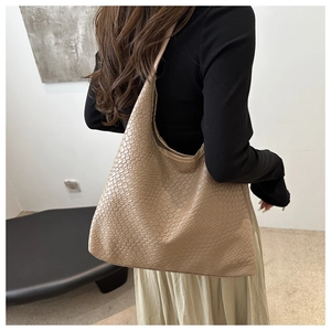 Close-up of beige woven texture tote bag worn by a model in a minimalist setting