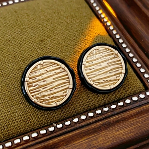 Close-up of golden round stud earrings with black enamel border and wood grain texture detail