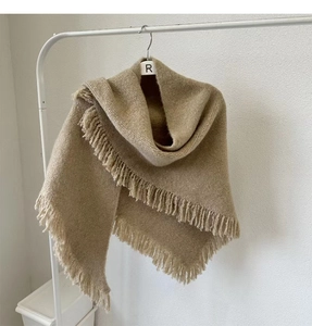 Detailed view of beige wool knitted shawl with fringe hanging on white hanger