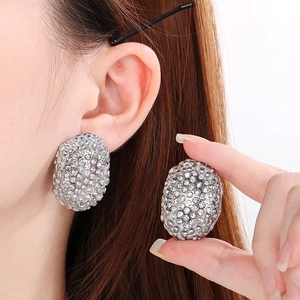 Close-up of oval silver earrings with pave-set rhinestones shown on a model