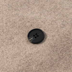 Detailed close-up of a black four-hole marble button on beige wool coat fabric