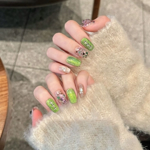 Short green cat-eye press-on nails with glitter sequins and pearl accents on hand