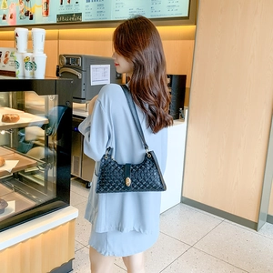 Chic black underarm bag with geometric embossing and gold lock shown in cafe setting