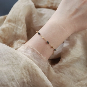 Dettaglio di un bracciale a catena dorata con perline blu scuro indossato sul polso