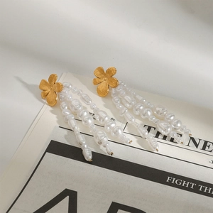 Dettaglio di orecchini a fiore dorato con eleganti nappe di perle barocche su giornale