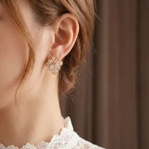 Elegant gold flower stud earrings with sparkling drop-shaped zirconias on ear