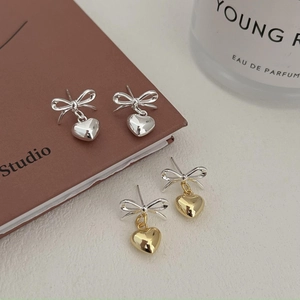 Detail of silver bow and heart stud earrings in silver and gold-tone finishes