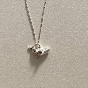 Macro shot of minimalist S925 sterling silver whale pendant necklace on beige texture