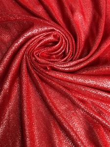 Macro detail of red glitter scarf fabric featuring a center spiral fold and shimmer