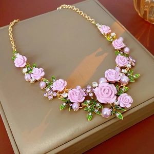 Détail de fleurs en résine rose et feuilles vertes sur un collier doré aux cristaux brillants