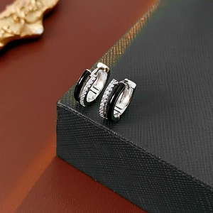 Detail of silver geometric hoop earrings with black enamel and clear zircon stones