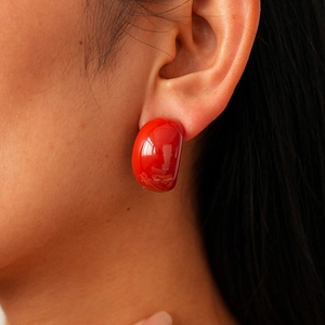 Detailed view of a glossy red hemispherical stud earring worn on the earlobe