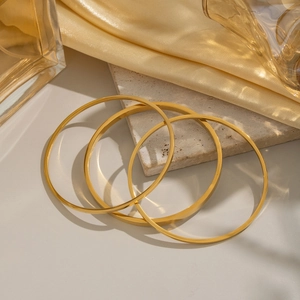 Dreiteiliges Set minimalistischer 18K vergoldeter geometrischer Armreifen auf Marmor