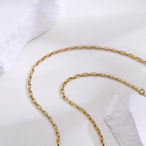 Detailed view of a golden stainless steel box chain necklace on a minimalist stone