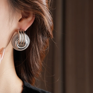 Close-up of chunky silver braided hoop earrings worn by a model for a stylish vintage look