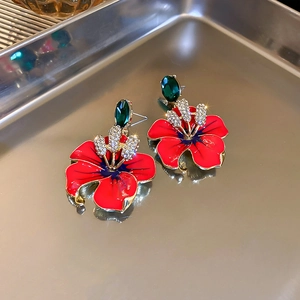 Detail of vintage orange flower earrings with red enamel petals and green gemstone accents