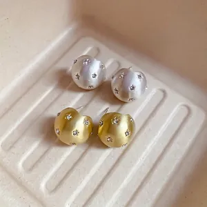 Star-patterned brushed metal stud earrings with cubic zirconia in silver and gold