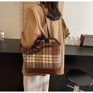 Detail view of large plaid tote bag with brown leather trim and metal buckle adjustment