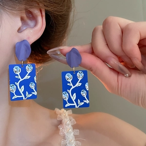 Detail of blue rectangular drop earring with purple petal top and white flower pattern