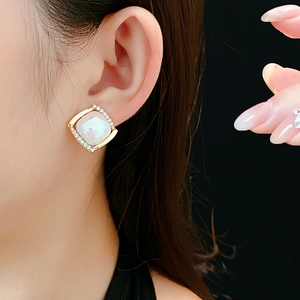 Détail de boucles d'oreilles carrées dorées avec cristaux et pierre blanche sur modèle
