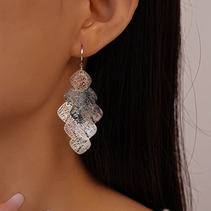 Close-up of silver hollow mesh diamond-shaped layered drop earrings worn by a model