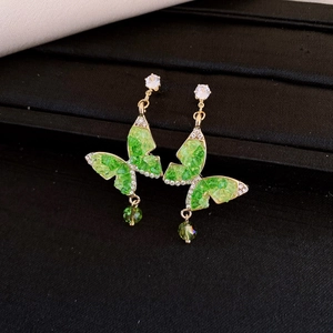 Gros plan de boucles d'oreilles papillon dorées avec pierres vertes et goutte de cristal