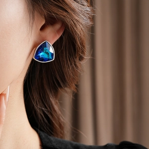 Gros plan d'un mannequin portant des boucles d'oreilles triangle en cristal bleu