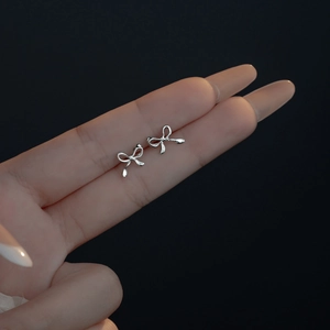 Silver bow stud earrings displayed on fingers against a minimalist black background