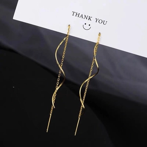 Détail de boucles d'oreilles vagues dorées avec de longues chaînes à pompons sur support