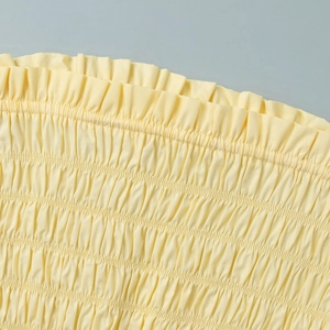 Close-up of the light yellow pleated fabric with elastic smocking texture and fine stitching