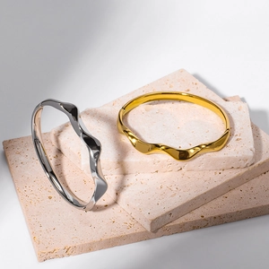 Minimalist Mobius wave bangles in gold and silver finish on modern stone display