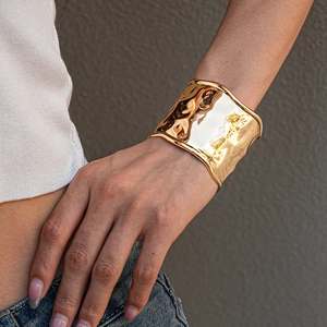 Detailed view of a wide gold cuff bracelet with hammered texture on a model's wrist